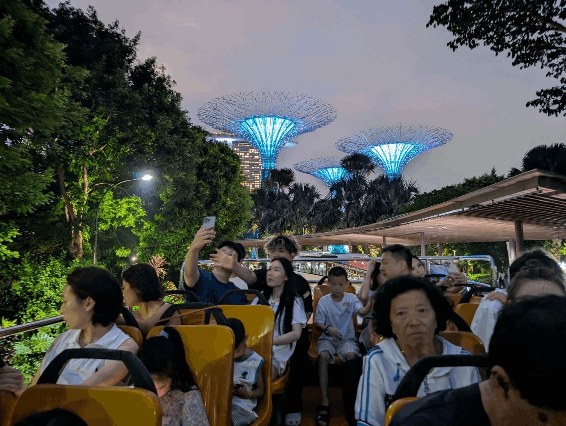 Families and passengers enjoying a FunVee Open-Top Night Tour with the illuminated Supertrees at Gardens by the Bay in the background.