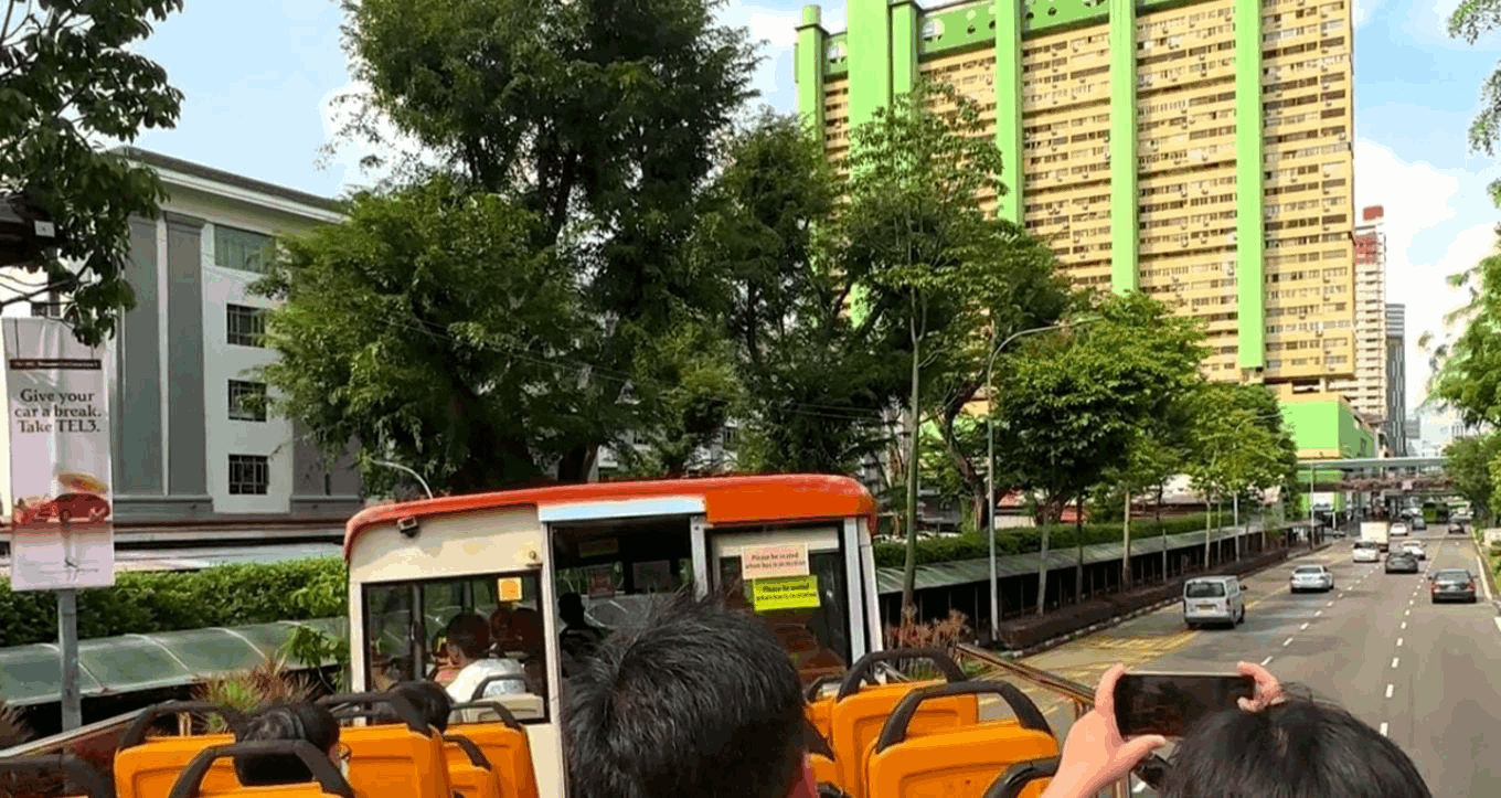 View from the FunVee open-top bus driving through Singapore towards Chinatown, with passengers taking photos and the iconic green People's Park Complex in the background.