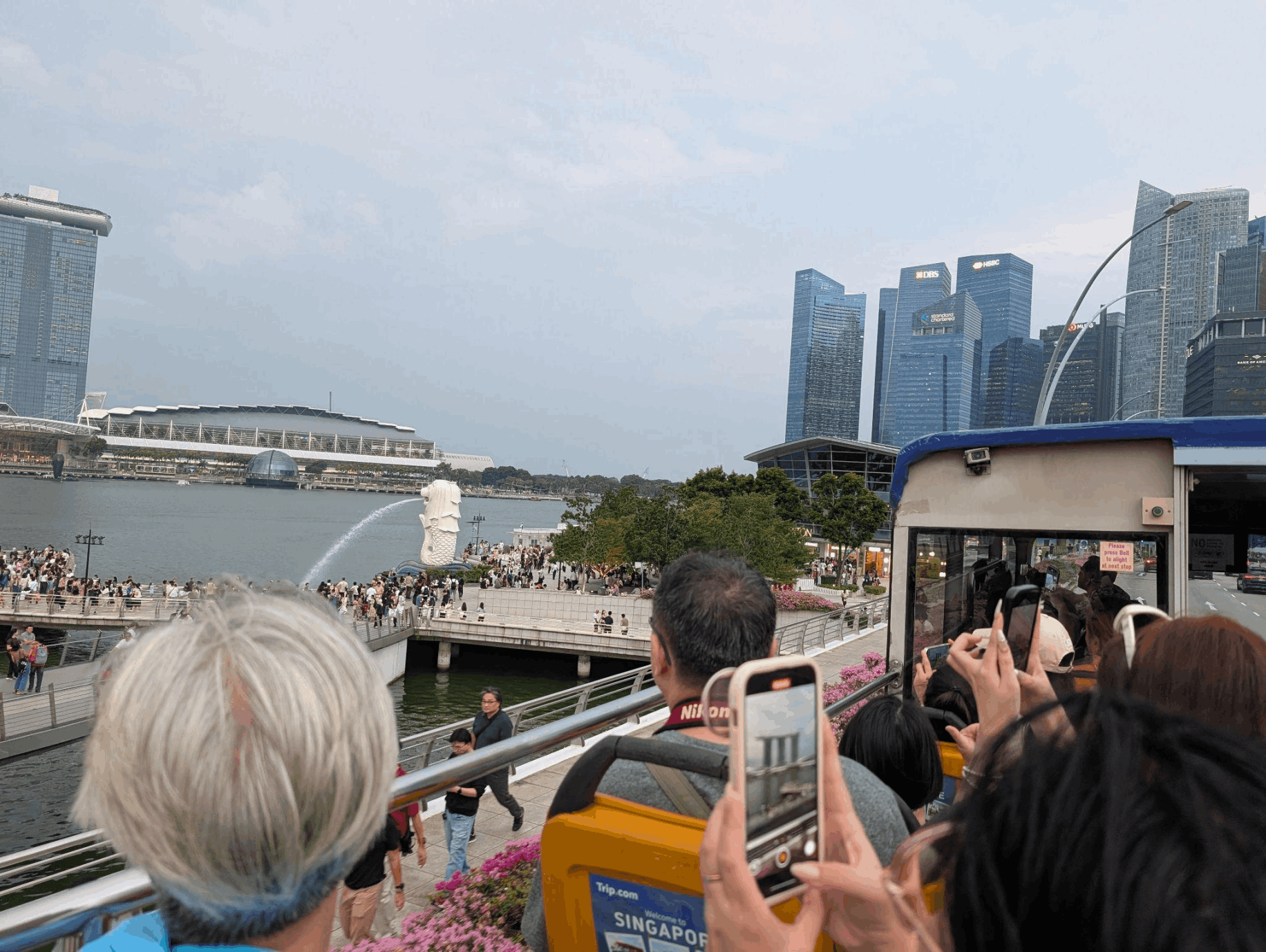 Passengers on a FunVee Open-Top Bus taking photos of the Merlion and Marina Bay skyline in Singapore.