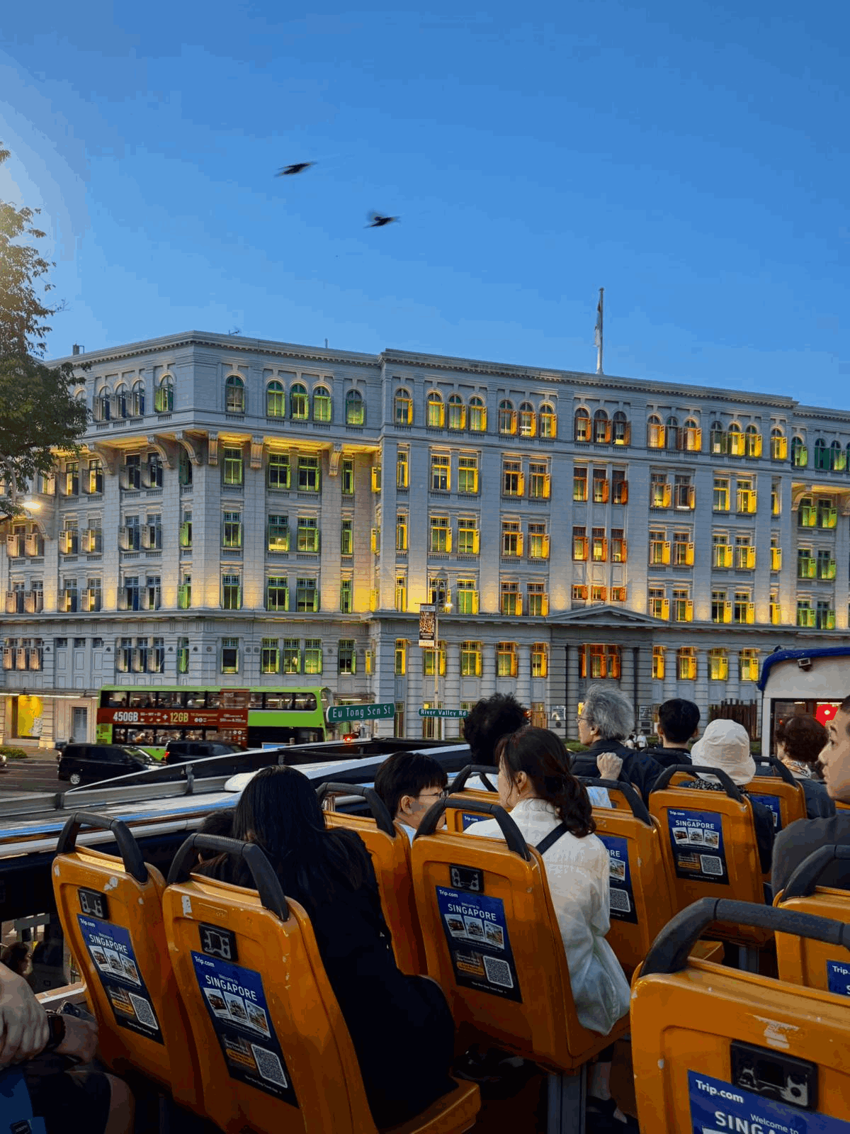 Tourists on the upper deck of the FunVee Open-Top Bus photographing the illuminated rainbow windows of Old Hill Street Police Station at night.