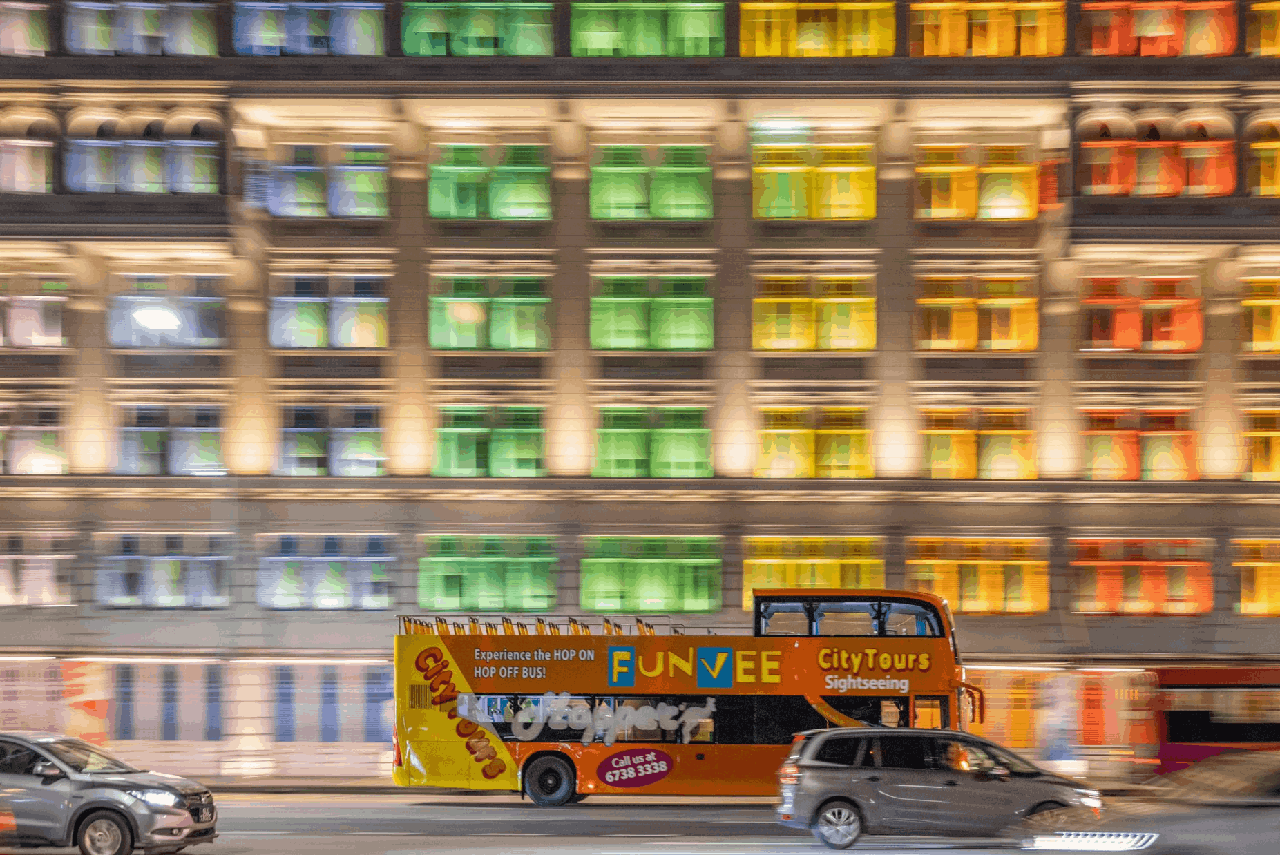 FunVee Open-Top Bus passing colourful city lights in Singapore at night, a scenic evening sightseeing tour for first-time visitors.