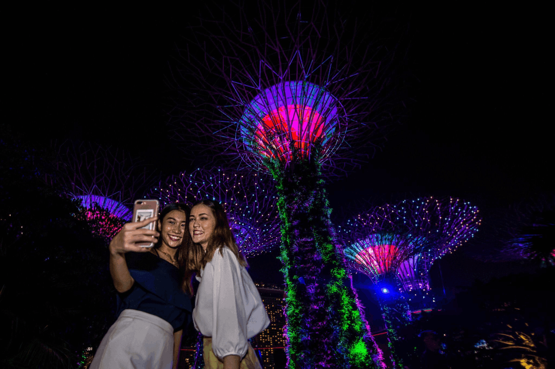 Travellers taking a selfie at the illuminated Supertree Grove at Gardens by the Bay, a popular free evening attraction in Singapore.