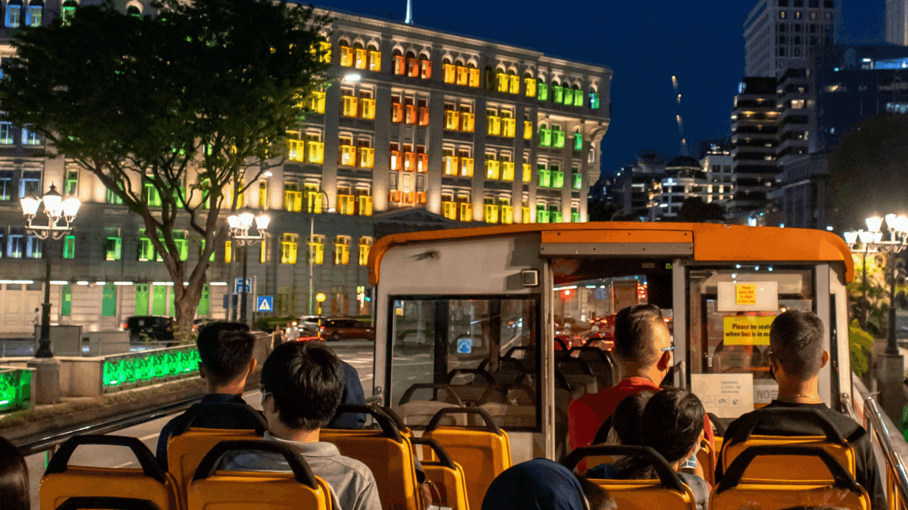 Tourists enjoying the breezy, elevated views of historic buildings from their seats on an open-top double-decker bus.