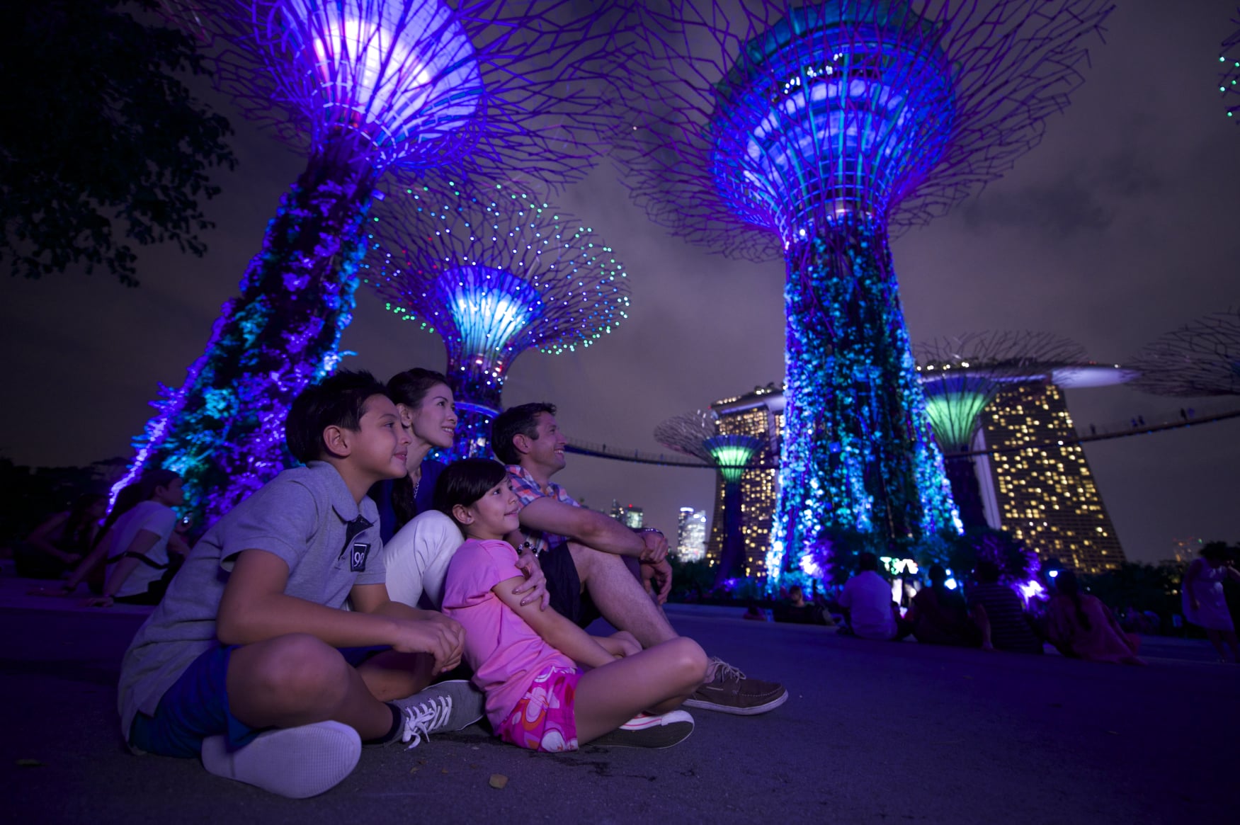 Night shot of a family sitting around the Supertrees Gardens by the Bay against the Marina Bay Sands Singapore