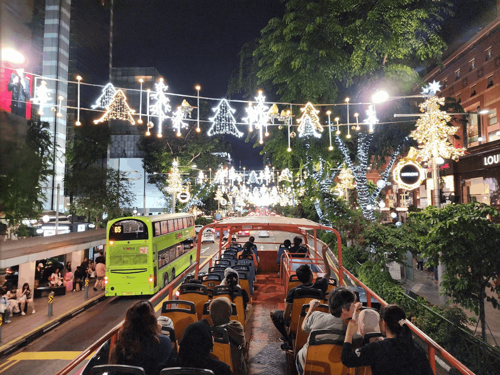 View from the back of an open-top tour bus, showing passengers enjoying the Orchard Road Christmas lights and traffic at night.