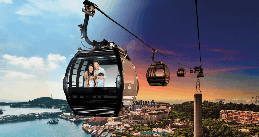 Singapore Cable Car cabin carrying a smiling family, with a scenic split view of the city and Sentosa Island — daytime on the left and sunset on the right, showcasing the skyline, coastline, and resorts below.