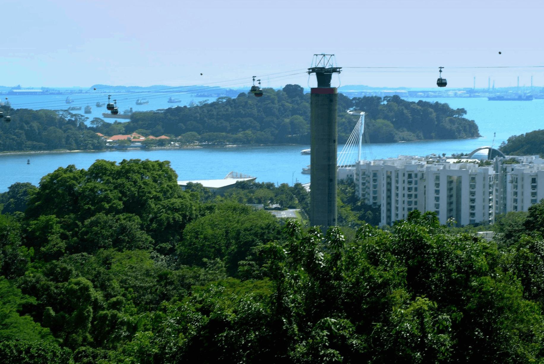Singapore Cable Car cabins travelling above the harbour with views towards Sentosa and the surrounding coastline.