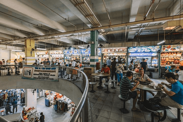 Diners enjoying meals at a bustling Singapore hawker centre, surrounded by food stalls offering a variety of authentic local dishes.